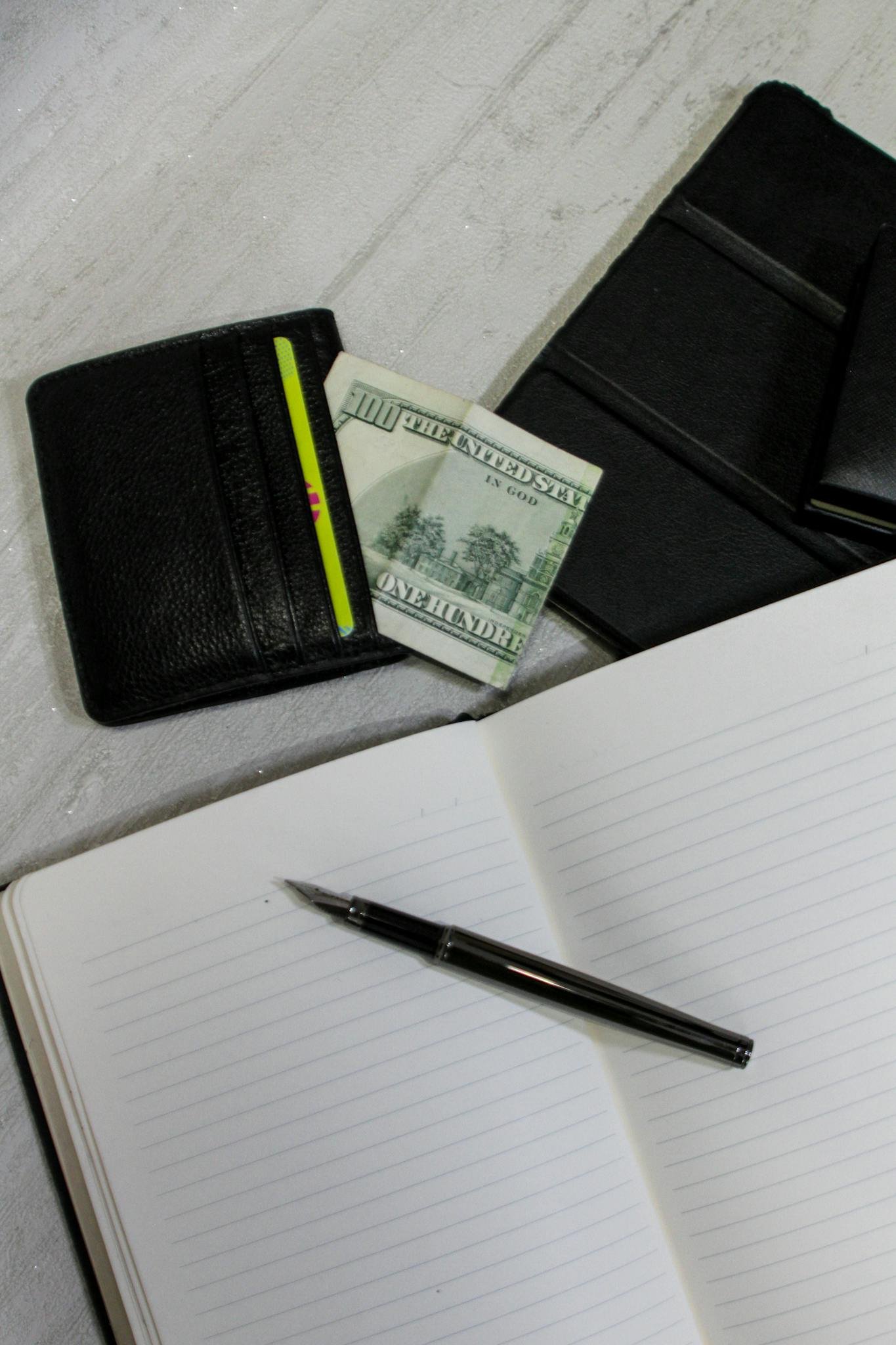 Top view of a wallet with cash, a notebook, and a pen on a white background, symbolizing financial planning.